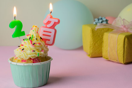 A birthday cupcake with 2-months candles, gifts and balloons on pink background.の写真素材