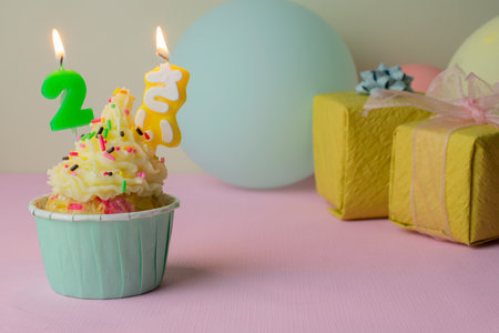 A birthday cupcake with 2-years candles, gifts and balloons on pink background.の写真素材