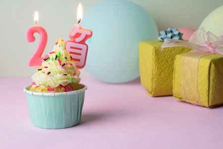 A birthday cupcake with 2-months candles and gifts on pink background.の写真素材