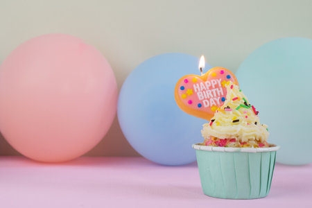 A birthday cupcake with happy birthday message candle and colorful balloons on pastel background.の写真素材