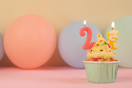 Birthday cupcake with two-years candles over pastel colored background.の写真素材