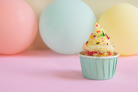 Birthday cupcake with colorful balloons on pastel pink background.の写真素材