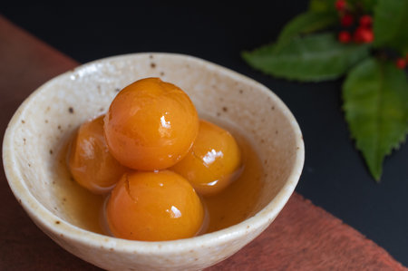 Closeup of Japanese confectionery, candied kumquats in a ceramic bowl with New Year decoration on black background.の写真素材