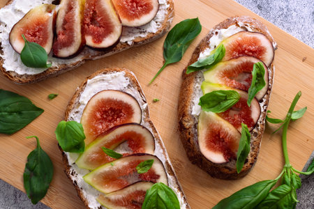 Open sandwiches with cream cheese, figs and basil on a wooden cutting boardの写真素材