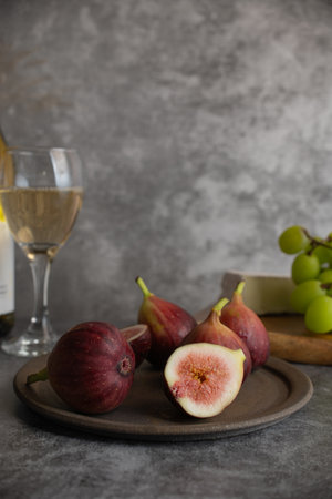 Ripe figs and a glass of white wine, a piece of cheese, and shine muscat on a gray marble backgroundの写真素材