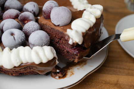 Chocolate cake with plums and whipped cream on a white plate placed on wooden tableの写真素材