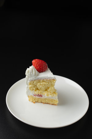 A slice of strawberry shortcake on a white plate with black backgroundの写真素材