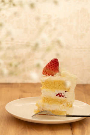 A slice of strawberry shortcake on a white plate placed on wooden table with blur backgroundの写真素材