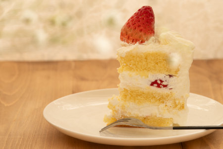 A slice of strawberry shortcake on a white plate placed on wooden table with blur background