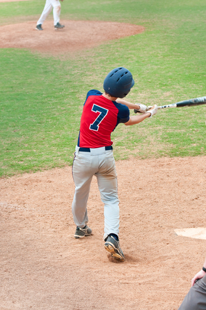 Teen boy swinging a baseball bat at the plate during a game.のeditorial素材