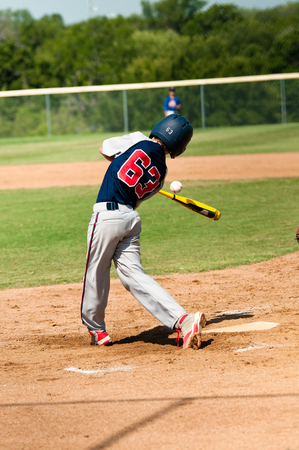 Young teen baseball batter in uniform swinging bat with referee in background.の写真素材