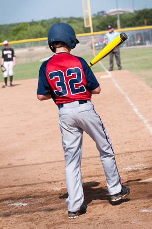 Young teen boy in red and blue baseball uniform batting with referee in background.