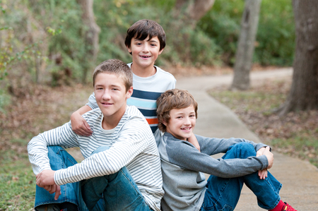 Group of three handsome boys that are family and friends sitting on sidewalk smiling at camera.の写真素材
