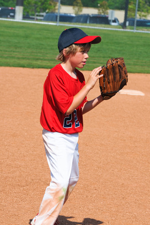 Young blonde hair baseball boy in red jersey holding glove.の写真素材