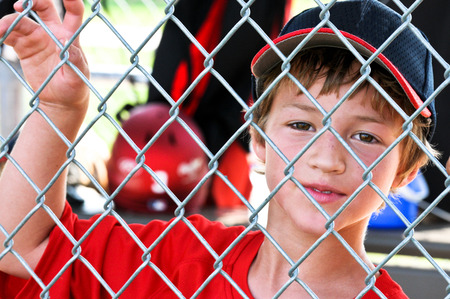 Upclose shot of a Little league baseball player standing in the dugout behind fence.の写真素材