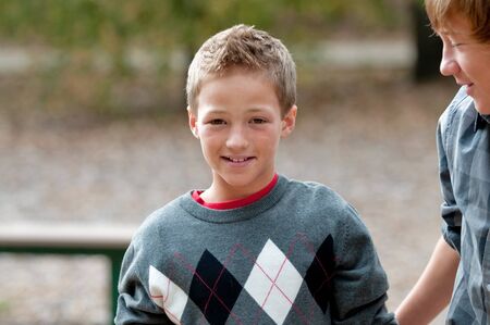 Cute young boy with smile on face, wearing sweater outdoors.
