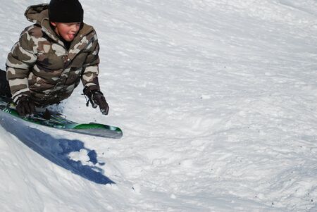 Little boy on a sled jumping a snowhill with tough out and copyspace to the right.の写真素材