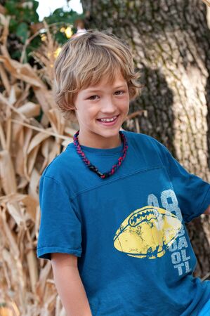 Portrait of adorable boy sitting in front of tree.