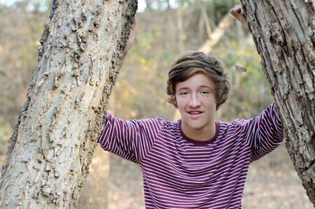 Portrait of cute teenage boy standing between trees outdoors.の写真素材
