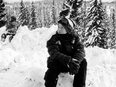 Boy in ski attire sitting on a pile of snow looking sideways.の写真素材