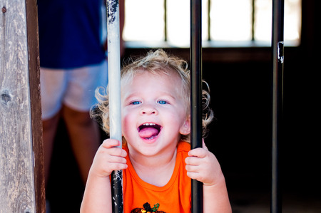 Close up of curly blonde haired toddler girl behind bars at a pumpkin festival.の写真素材