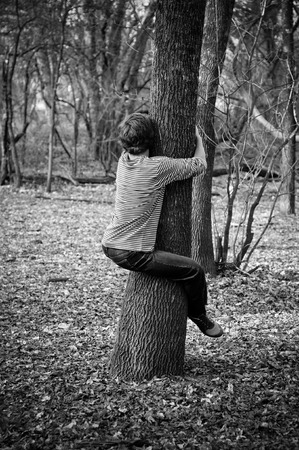 Black and white photo of teenage boy tree hugging.の写真素材