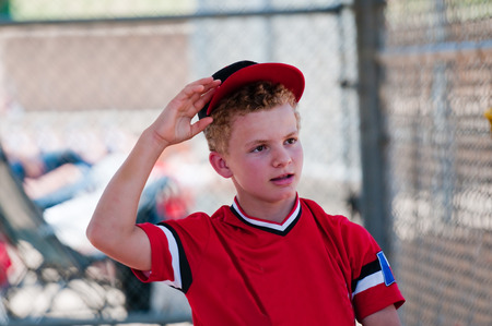 Teenage baseball boy in dugout reaching for ball cap.の写真素材