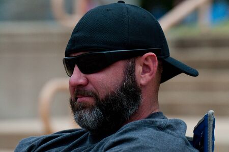 Middle-aged man with black and grey beard wearing sunglasses and hat backwards.の写真素材