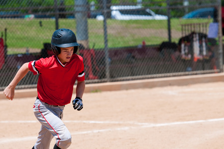 Youth teenage baseball kid running to first base.