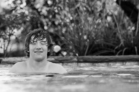 Black and white photo of handsome teenage boy with eyes closed and braces on teeth standing in blue swimming pool.の写真素材