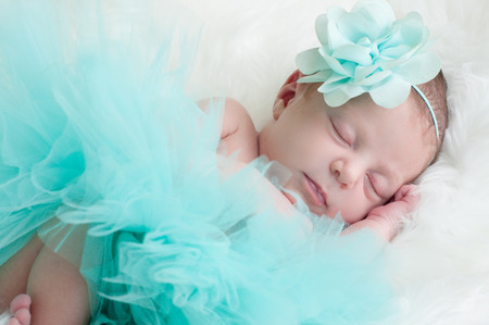 Precious baby girl sleeping in teal outfit laying on white fur.の写真素材
