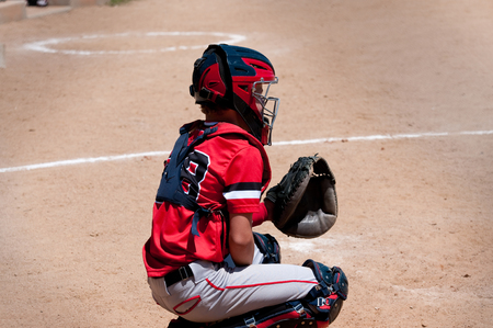 American youth baseball catcher behind home plate waiting on pitch.