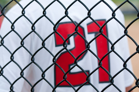Close up of a baseball fence with white  uniform in background.の写真素材