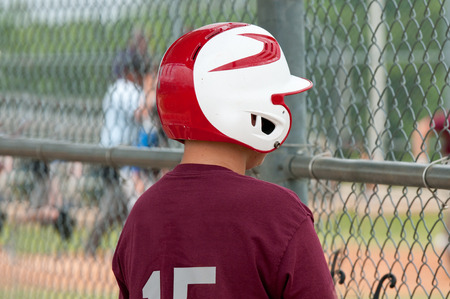 Little league baseball boy looking through dugout fence with red helmet.