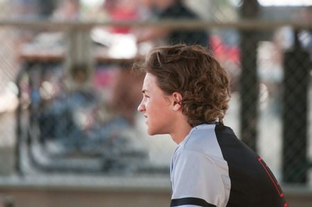 Youth baseball boy sitting in dugout looking sideways.の写真素材