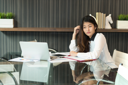 Asian woman thinking about work in front of laptop in modern meeting roomの写真素材