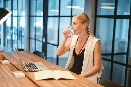 Business blonde girl drinking water in front of a laptopの写真素材
