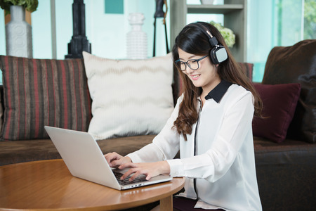 An Asian business woman listening to songs, relaxing music, using headphonesの写真素材