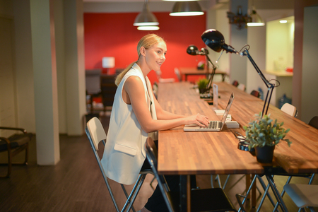 Business blonde girl working late, using a laptop in an officeの写真素材