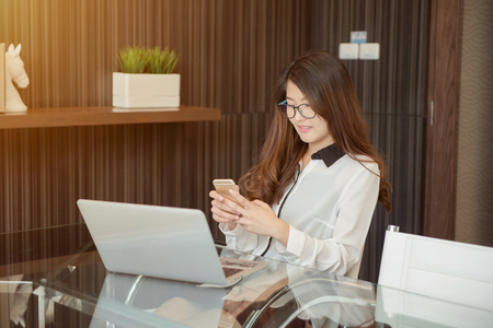Asian business woman using a phone in front of a laptopの写真素材