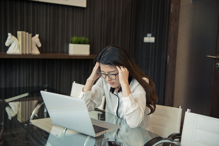 A Stressed Asian business woman using a laptop in officeの写真素材
