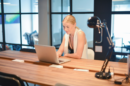 Happy business blonde girl using a laptop in an officeの写真素材
