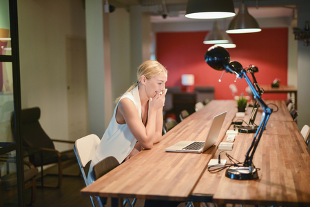 Happy business blonde girl using a laptop in an officeの写真素材