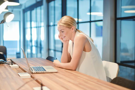 Happy business blonde girl using a laptop in an officeの写真素材
