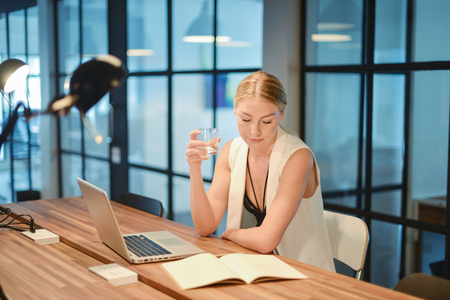 Business blonde girl drinking water in front of a laptopの写真素材