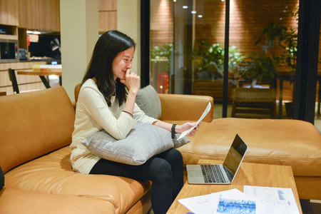 Business woman using a laptop with business documents in living room at nightの写真素材