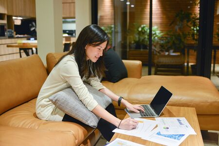 Business woman using a laptop with business documents in living room at nightの写真素材