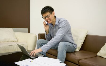 Stressed Asian businessman using a smartphone in living room at nightの写真素材