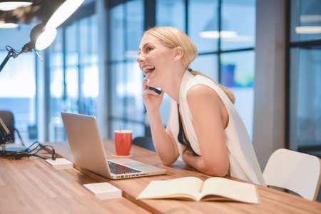 Business blonde woman taking on the phone and laughing in front of a laptopの写真素材