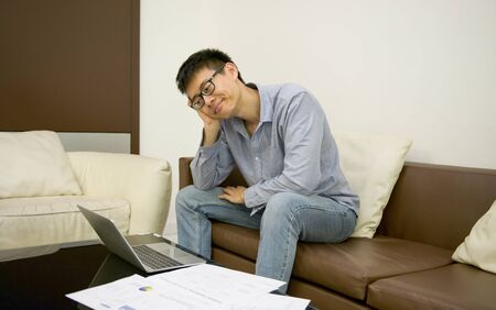 Stressed Asian businessman using a smartphone in living room at nightの写真素材